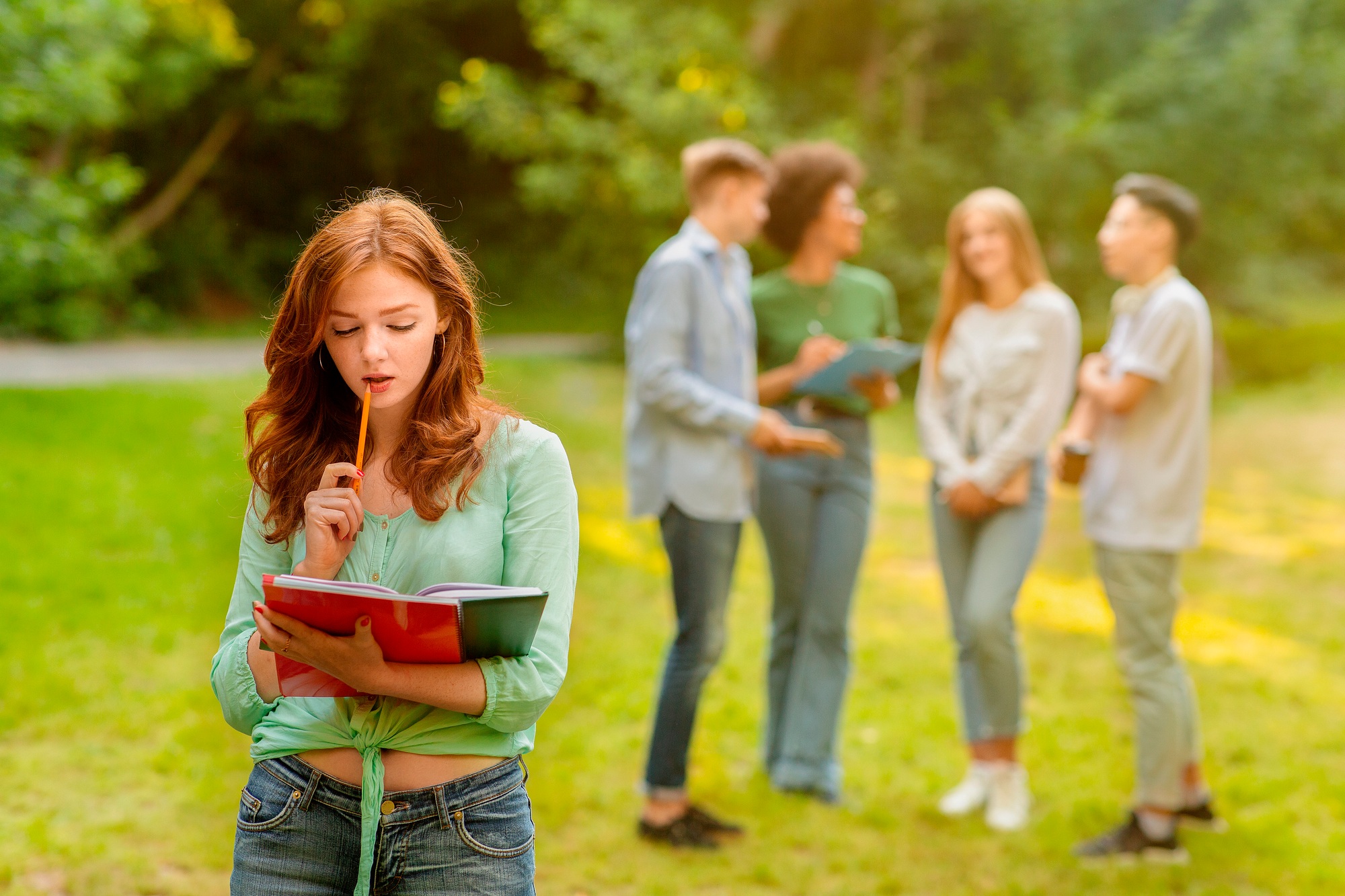 Education First. Student Girl Preparing For Exam Outdoor While Her Classmates Chatting